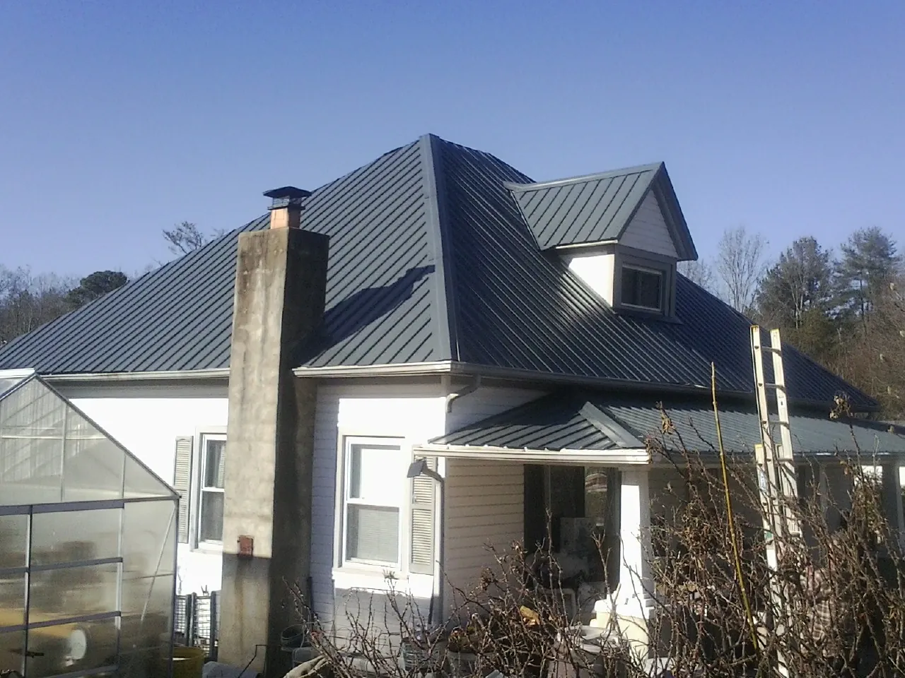 Dark blue standing seam metal roof on a white farmhouse with dormer — Slate & Tile Roof Repair by Roofing Brothers in Davis Junction