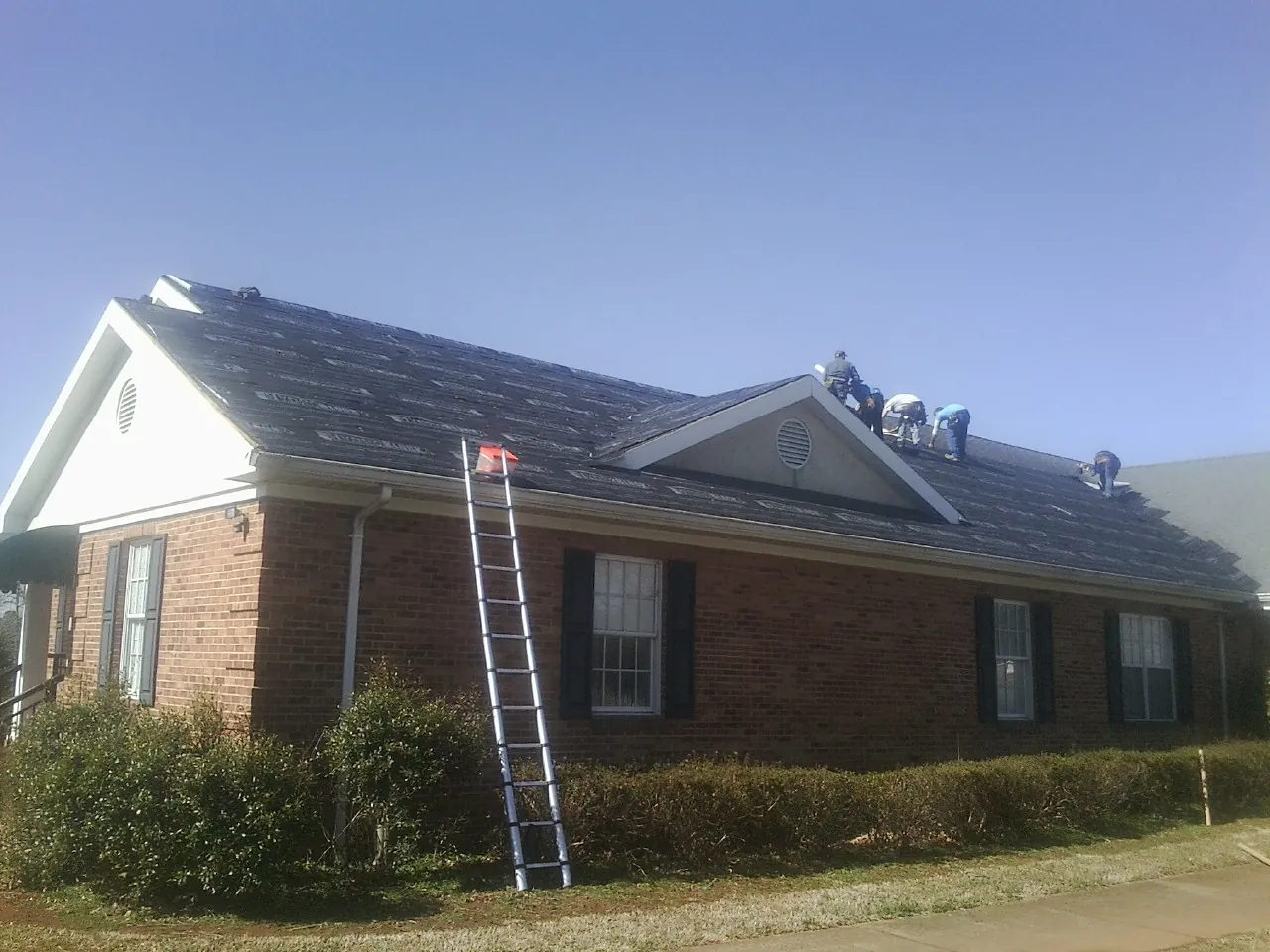 Crew tearing shingles off a brick ranch roof with a ladder set — Emergency Roof Repair work by our crew in Davis Junction