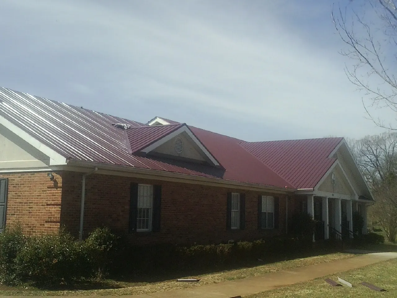 Red metal roof with gabled entries on a long brick building, from a Hail Damage Roof Repair job in Davis Junction