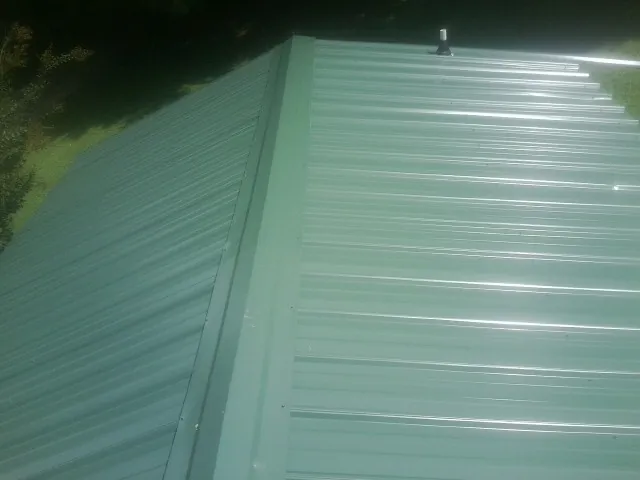 New green metal panels meeting at the ridge of a roof — Flat Roof Repair work by our crew in Davis Junction